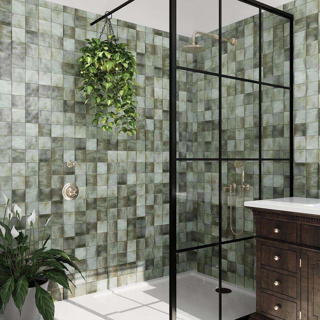 A contemporary styled bathroom featuring a walk-in shower enclosed with black-framed glass, variegated green tiles, and a hanging plant adding a touch of nature