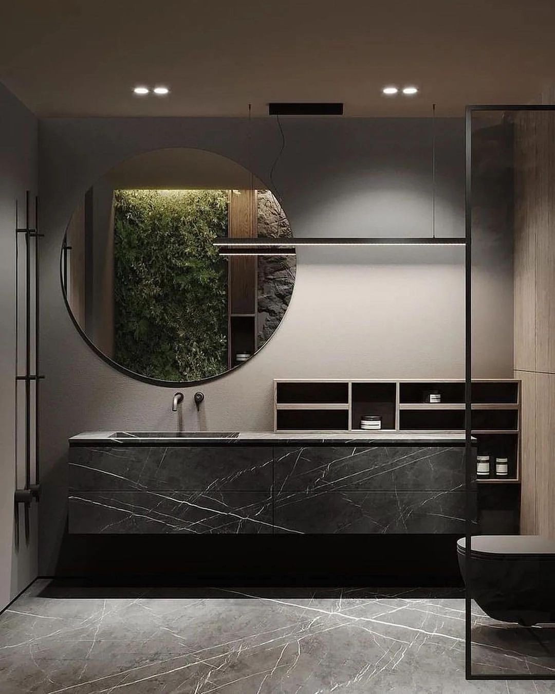 A modern gray-toned bathroom featuring a circular mirror reflecting lush greenery, a sleek marble basin, and a wooden vanity with minimalist shelving.