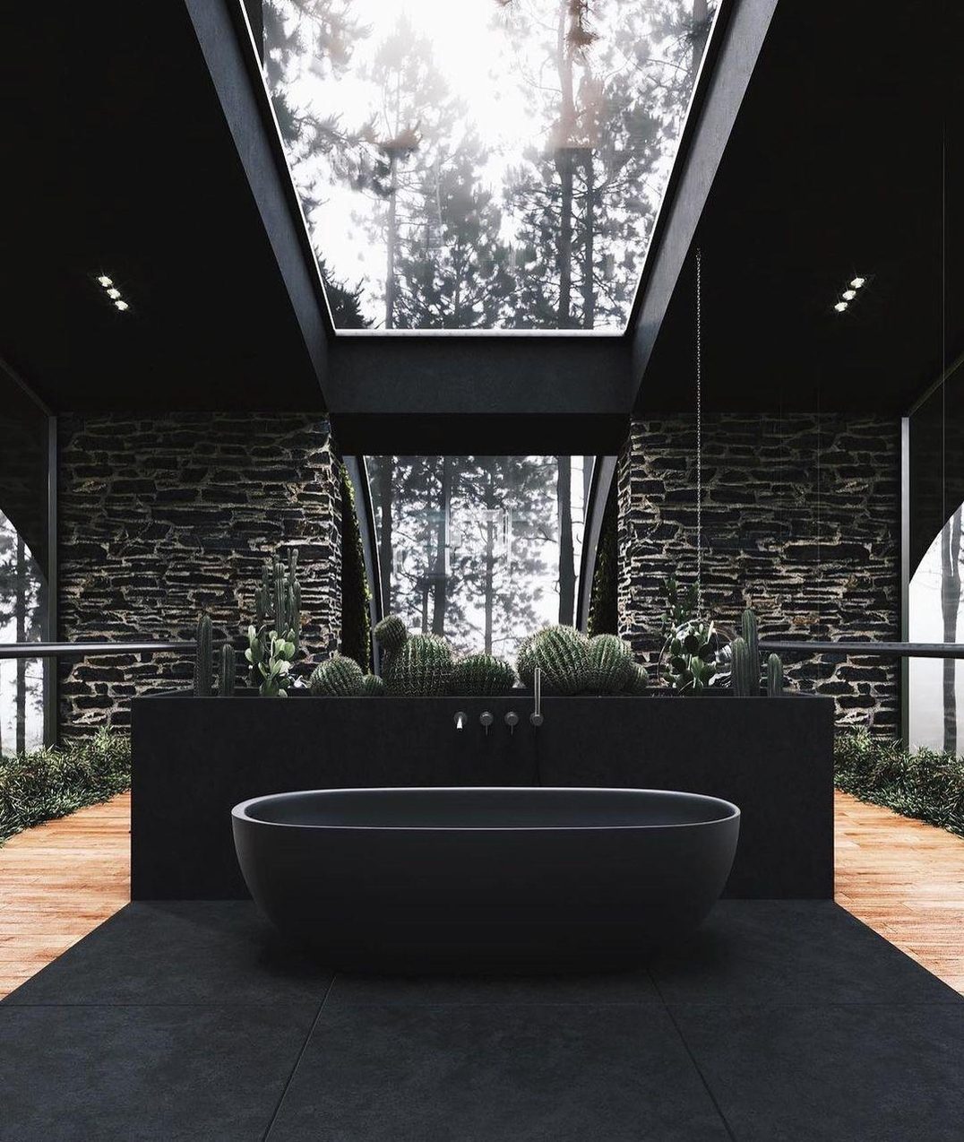 A contemporary bathroom featuring a free-standing bathtub in front of a stone wall, with a modern vanity adorned by cacti, set against floor-to-ceiling windows with a forest view