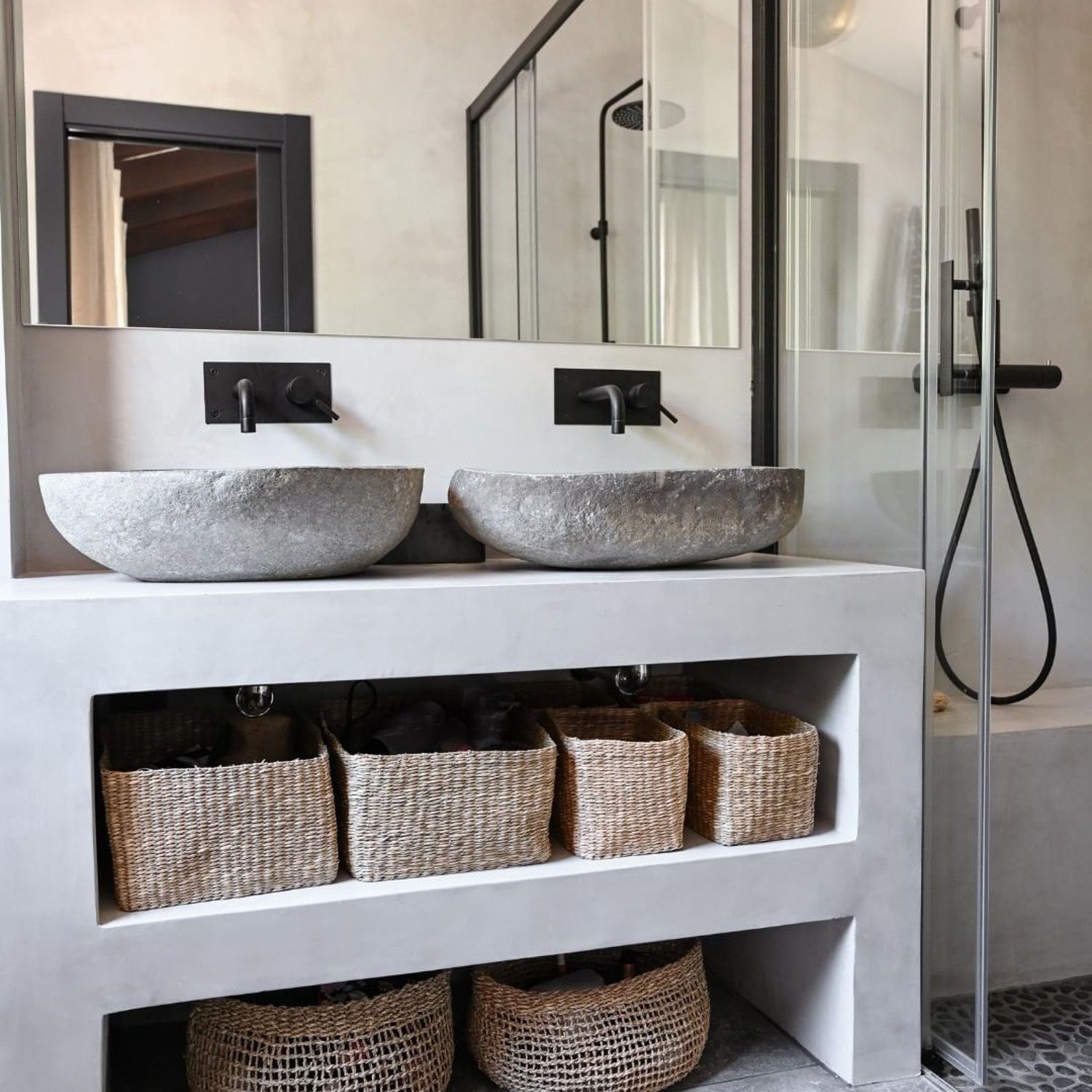 A chic bathroom featuring textured stone basins and woven organizational baskets.