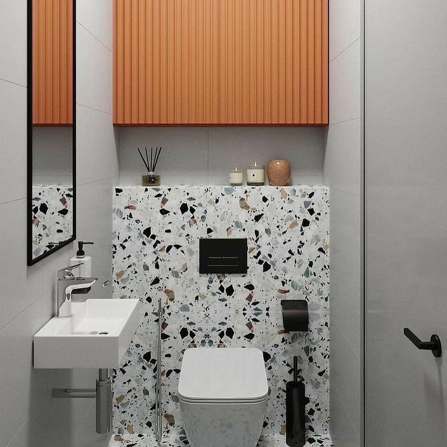 A modern bathroom featuring terrazzo tiles, a wall-mounted sink, and a bold orange linear panel above.