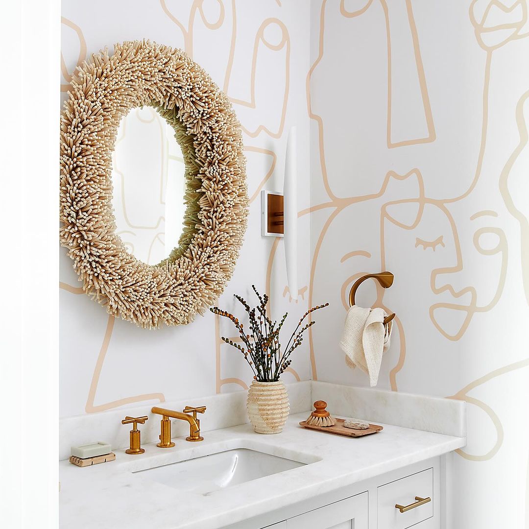 A chic modern bathroom featuring a unique shell-style mirror and whimsical line-drawn wallpaper