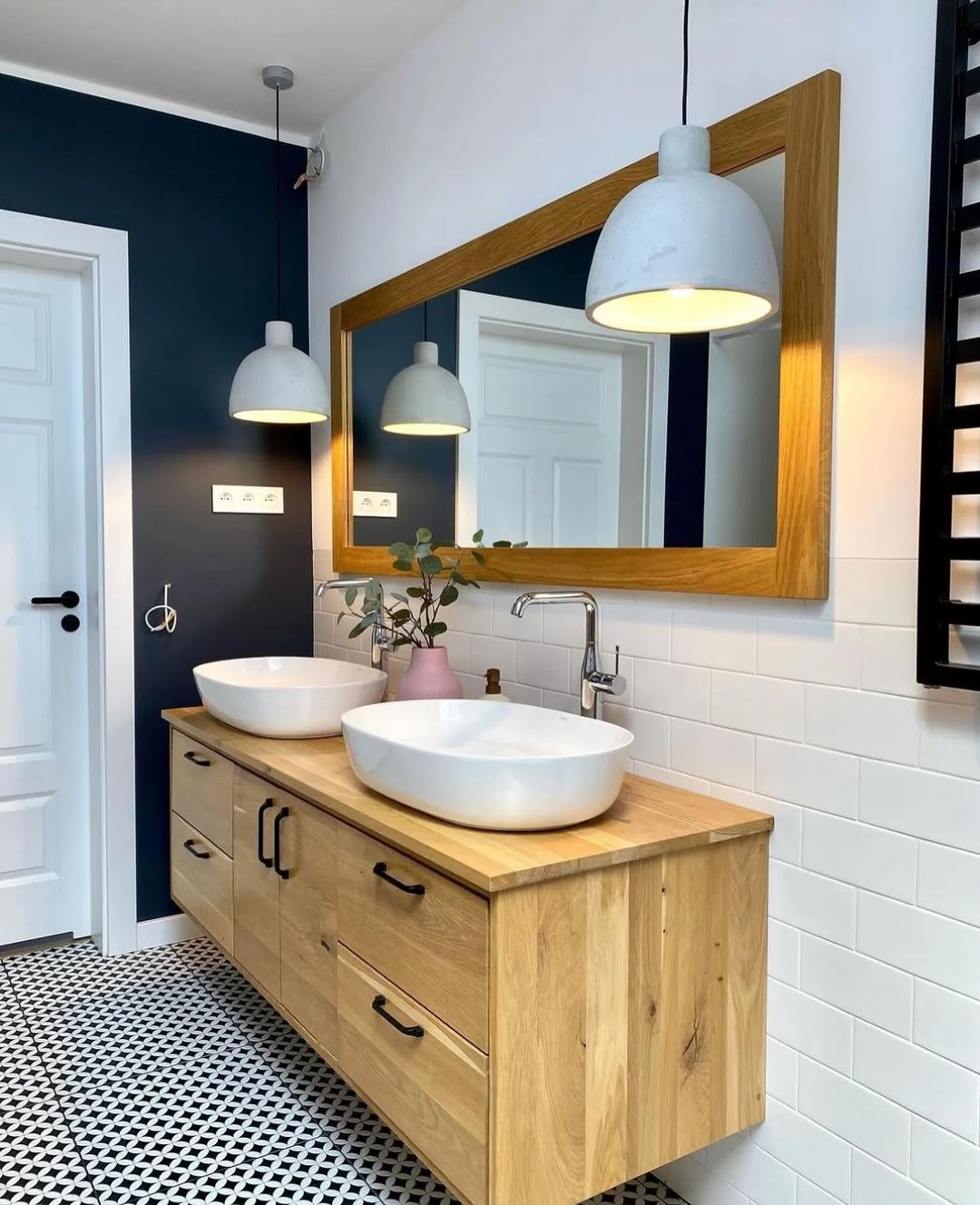 A contemporary bathroom featuring dual vessel sinks atop a wooden vanity, against a bold navy blue wall and geometric tiled flooring.