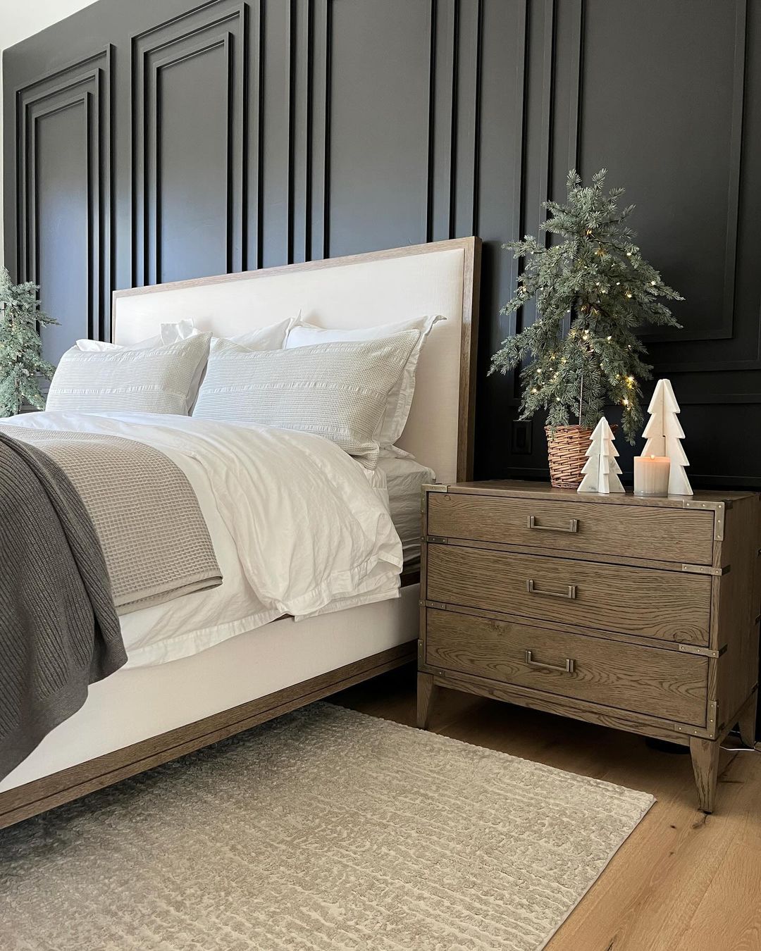 A chic bedroom boasts a striking contrast with black paneled walls, a beige upholstered bed, and natural wood accents.