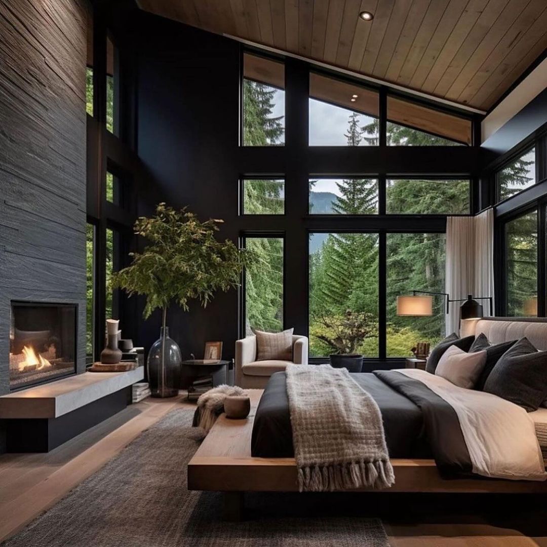 A modern and sophisticated bedroom featuring expansive windows overlooking a lush forest, black textured walls, and a cozy fireplace