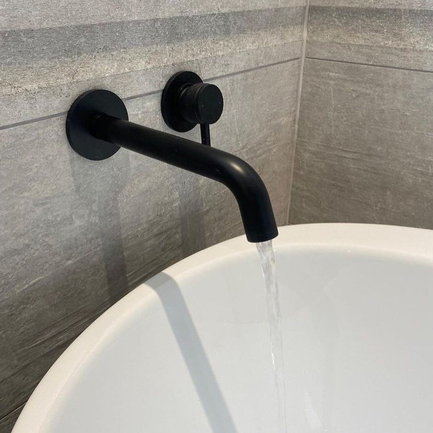 A minimalist black faucet with water flowing into a white basin