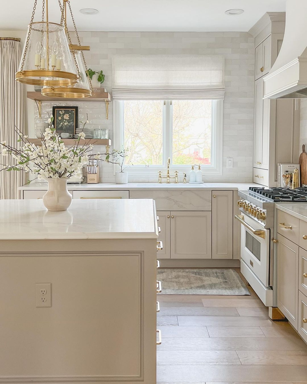 A chic, modern kitchen featuring a brass pendant light over a marble-top island, white shaker cabinets, and high-end stainless steel appliances