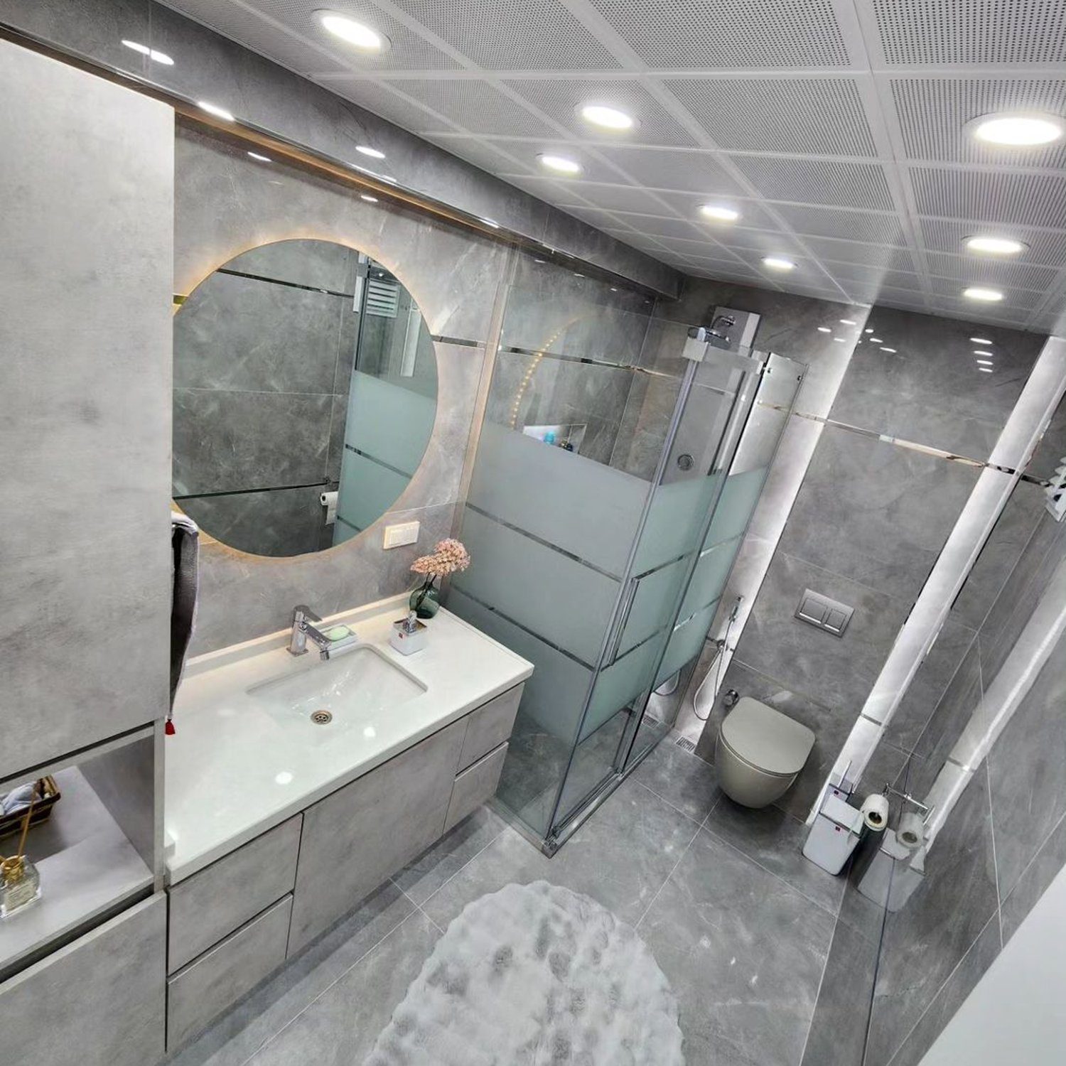 A modern and sleek bathroom featuring gray tones, large mirror, and glass shower enclosure.