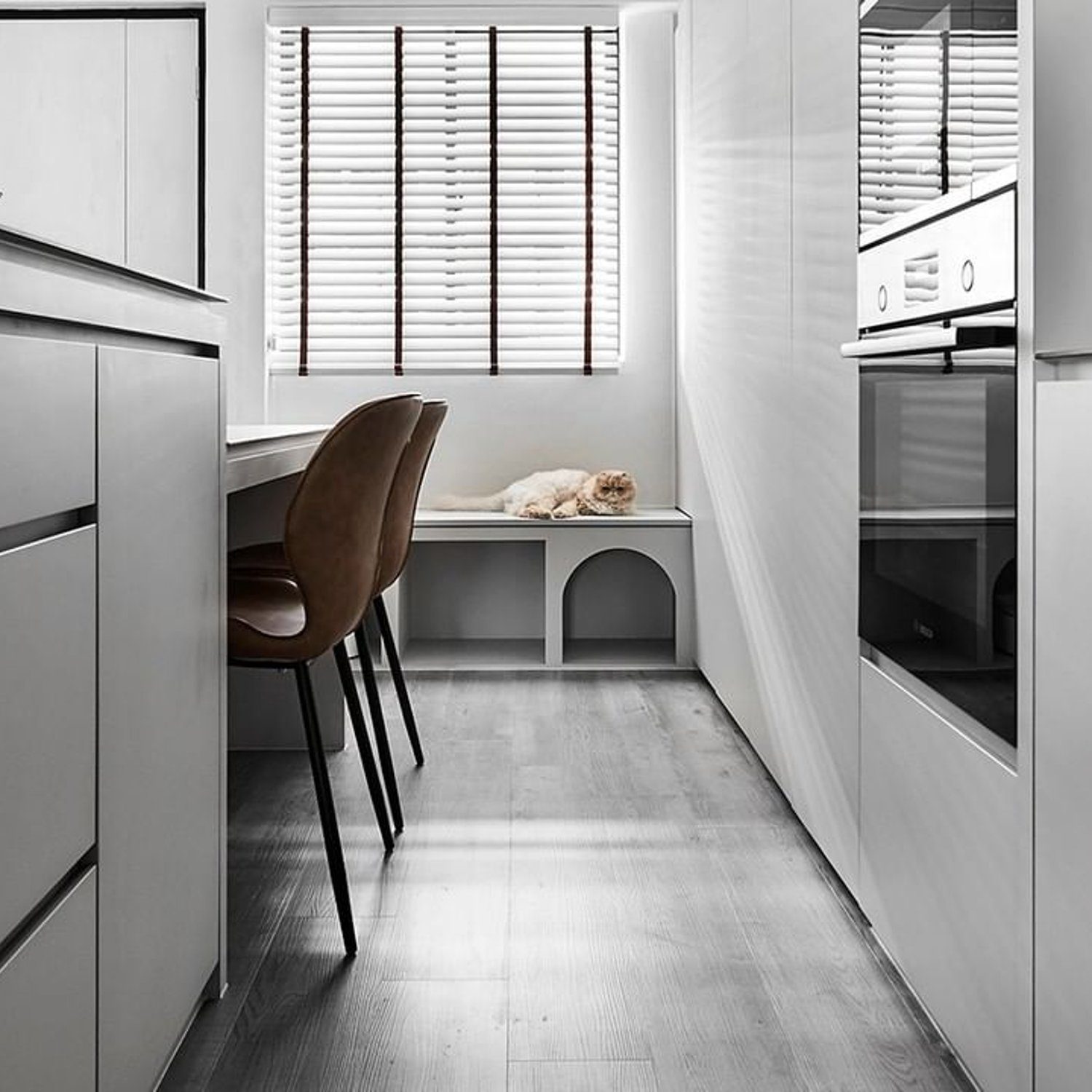 A sleek and modern kitchen in shades of grey with a touch of warmth from a brown chair