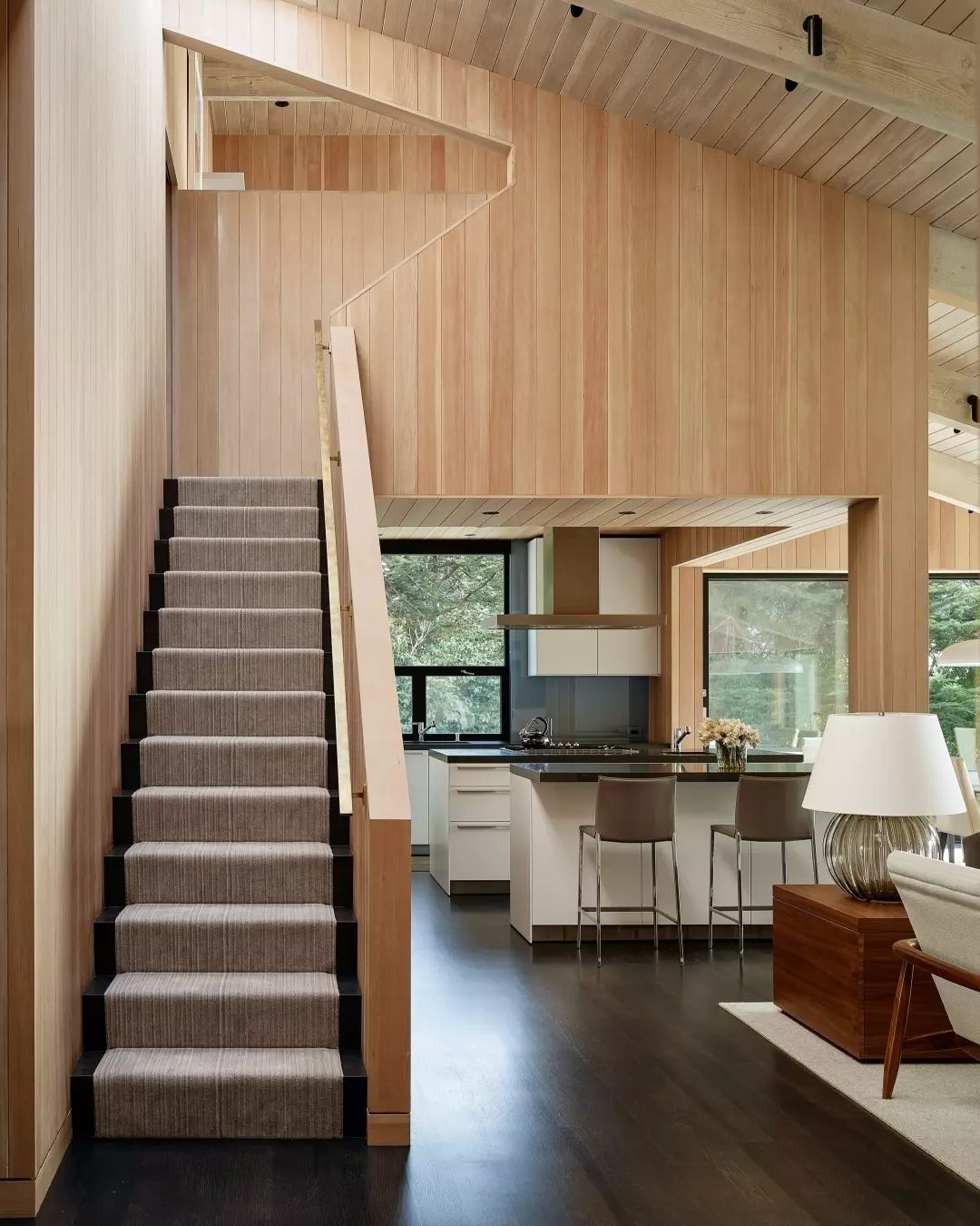 A modern and homely interior design featuring a straight staircase with carpeted steps leading to an upper level, positioned adjacent to a sleek kitchen area