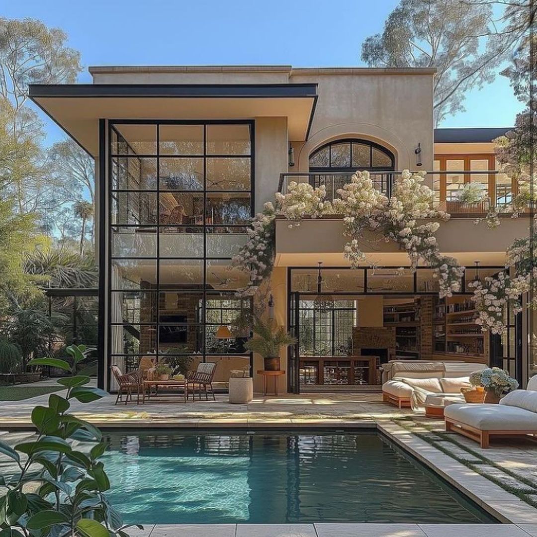 A modern two-story house with expansive glass walls overlooking a serene pool.