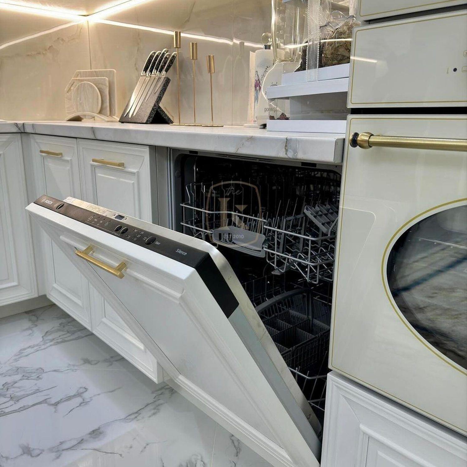 A luxurious kitchen featuring a dishwasher integrated into ornamental white cabinetry, complemented by marble countertops and stylish golden accents.