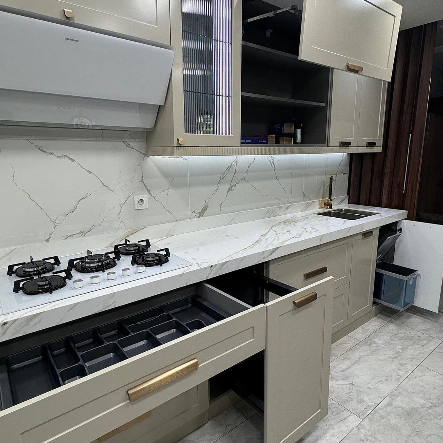 A meticulously designed modern kitchen with beige cabinetry, marble countertops and backsplash, and stainless steel appliances.