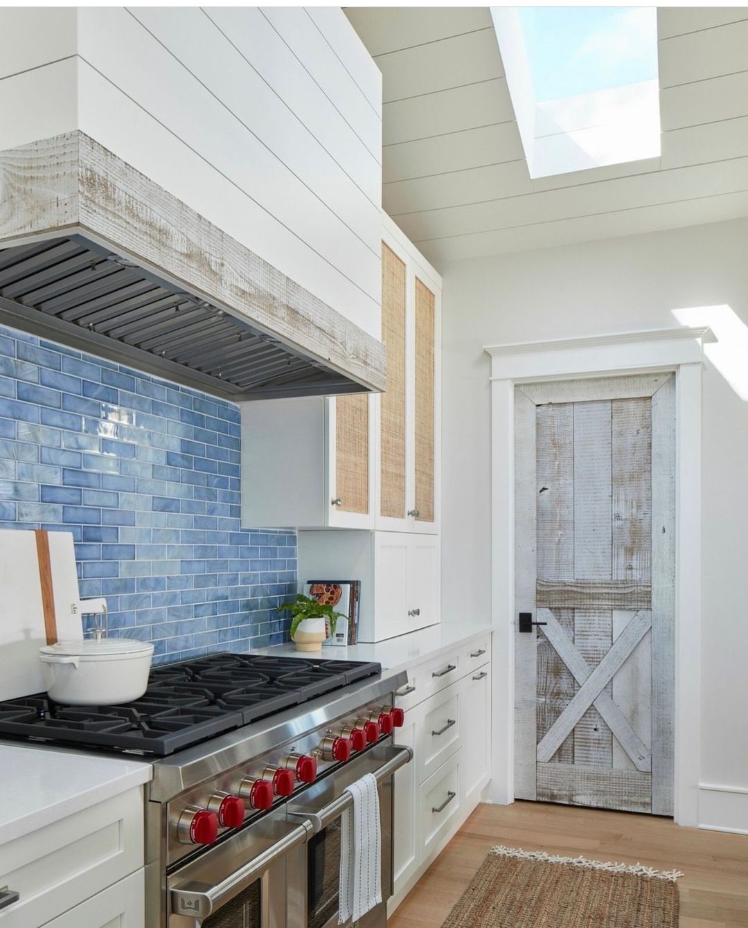 A modern kitchen featuring a bold blue tile backsplash, sleek stainless steel range with red knobs, and a distinctive sliding barn door