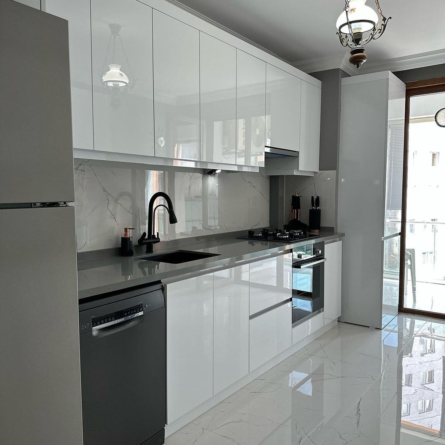 A modern, sleek kitchen with high-gloss white cabinetry and marble-like tiles