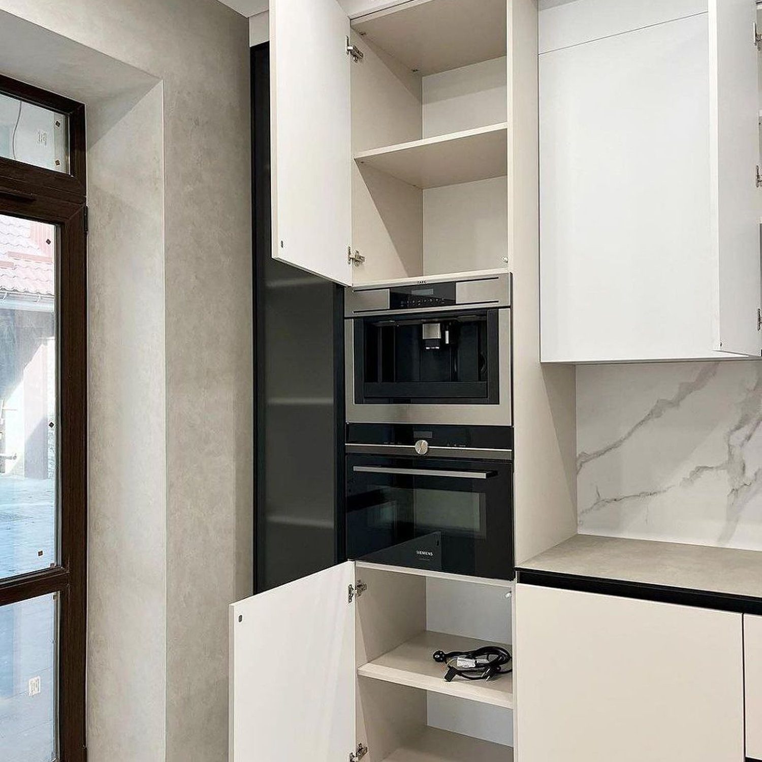 A sleek and modern kitchen corner featuring marble countertops, glossy white cabinetry, and high-end built-in appliances