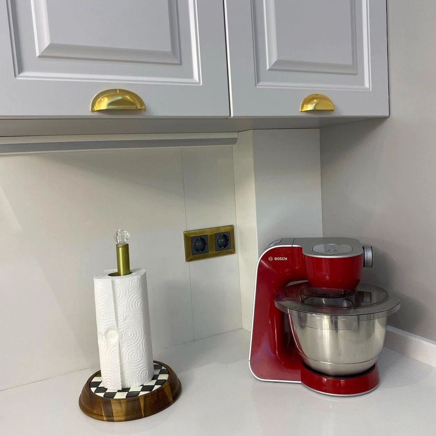 A modern kitchen corner featuring a red Bosch mixer and a paper towel holder on a checkered stand