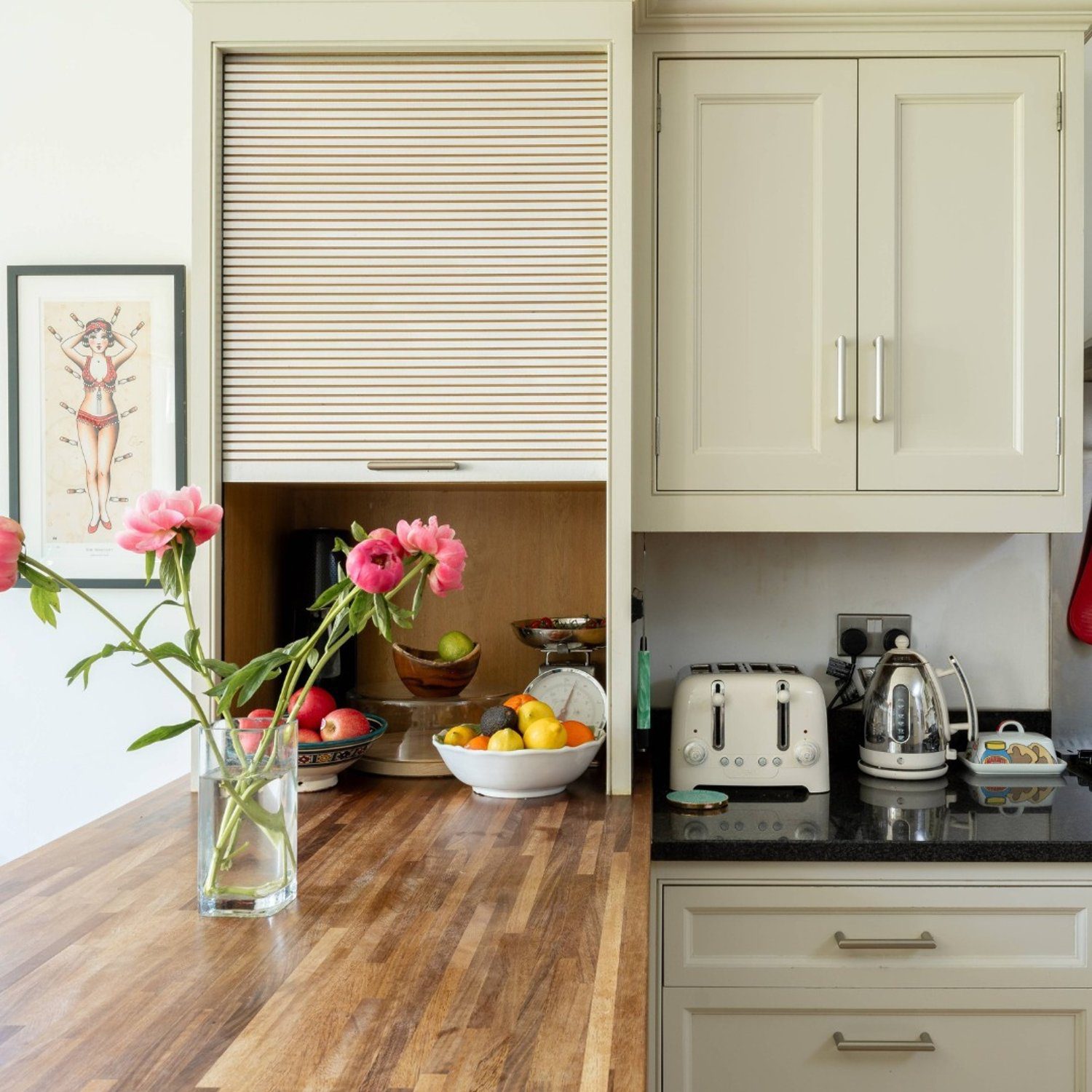 A neatly organized kitchen corner with beige cabinetry and a vibrant touch of pink from the fresh flowers.