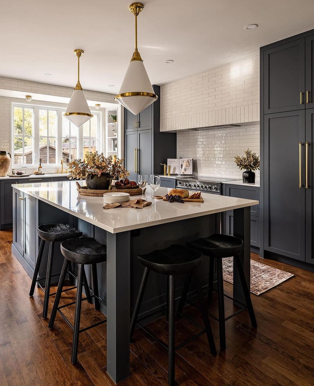 A modern kitchen featuring sleek dark cabinetry, white countertops, and brass accents