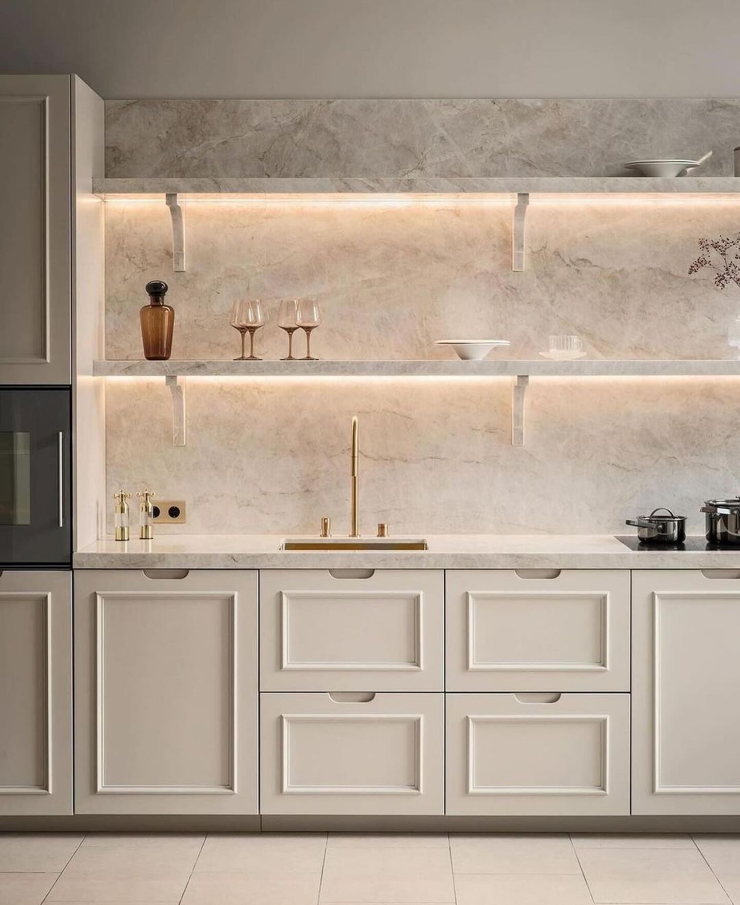 A modern kitchen with creamy cabinets and marble walls and backsplash