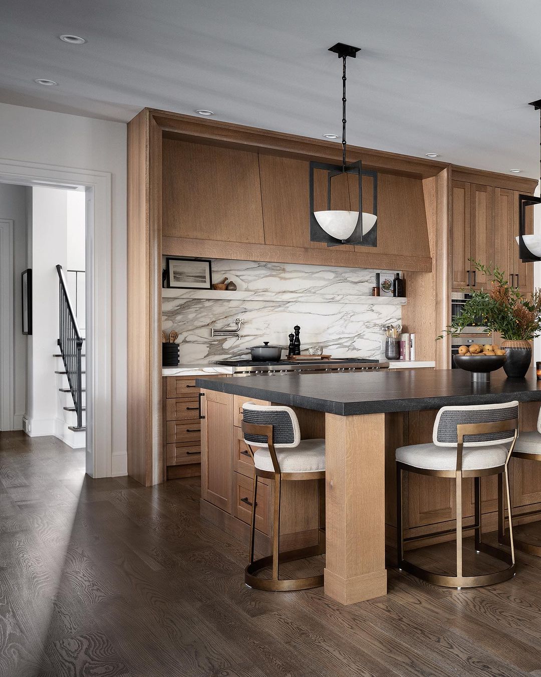 A modern kitchen design with warm wood cabinets, marble backsplash, and a sleek dark island