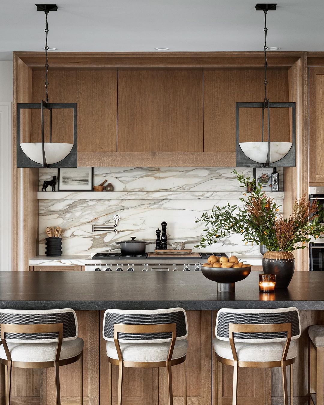 A sleek and modern kitchen featuring wood cabinetry, marble backsplash, and chic barstools