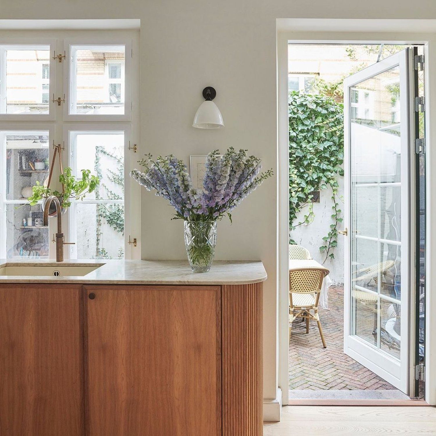 A modern kitchen with a wooden cabinet and marble countertop, featuring a vase with lavender flowers.