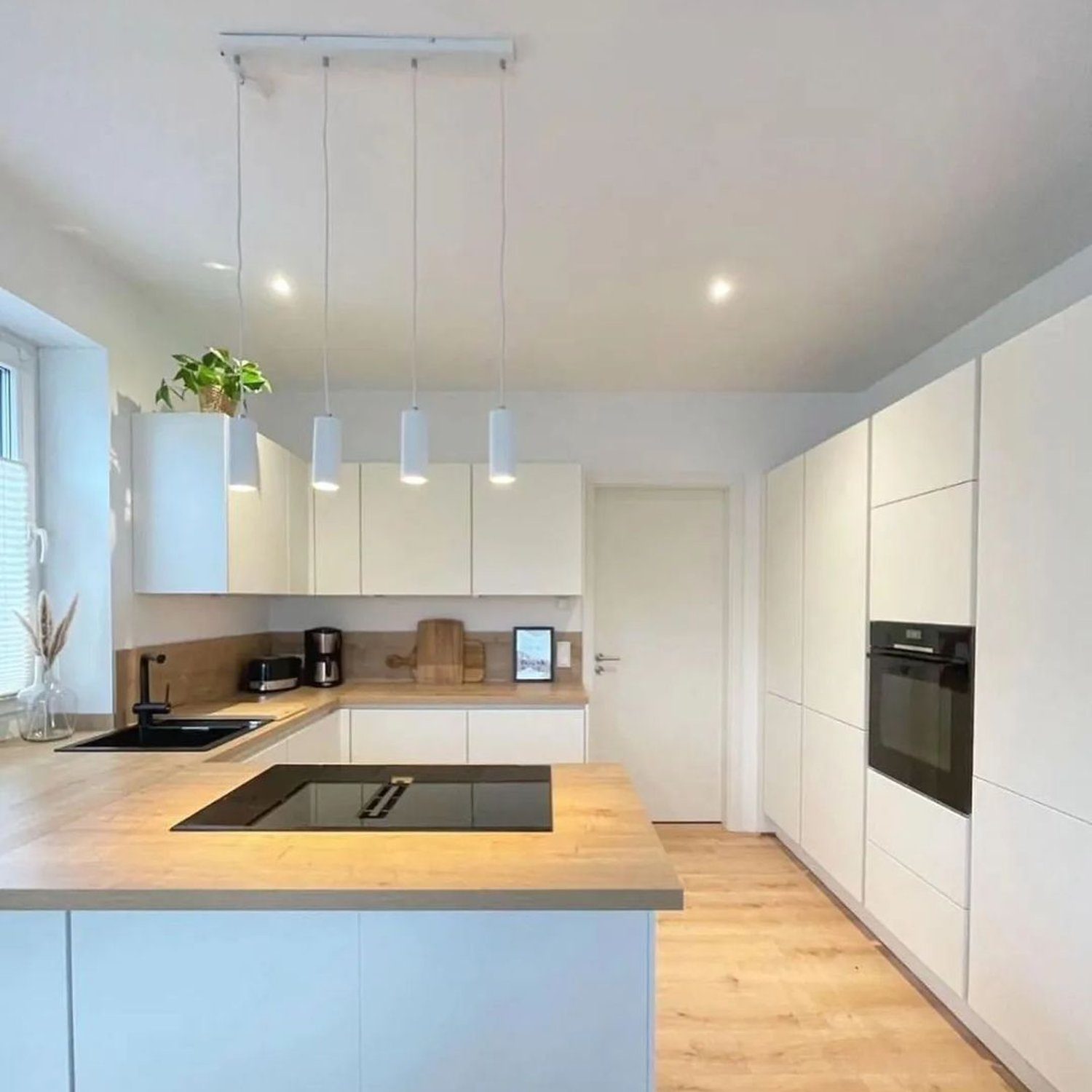 A modern and sleek kitchen design featuring white cabinetry, wood accents, and pendant lighting