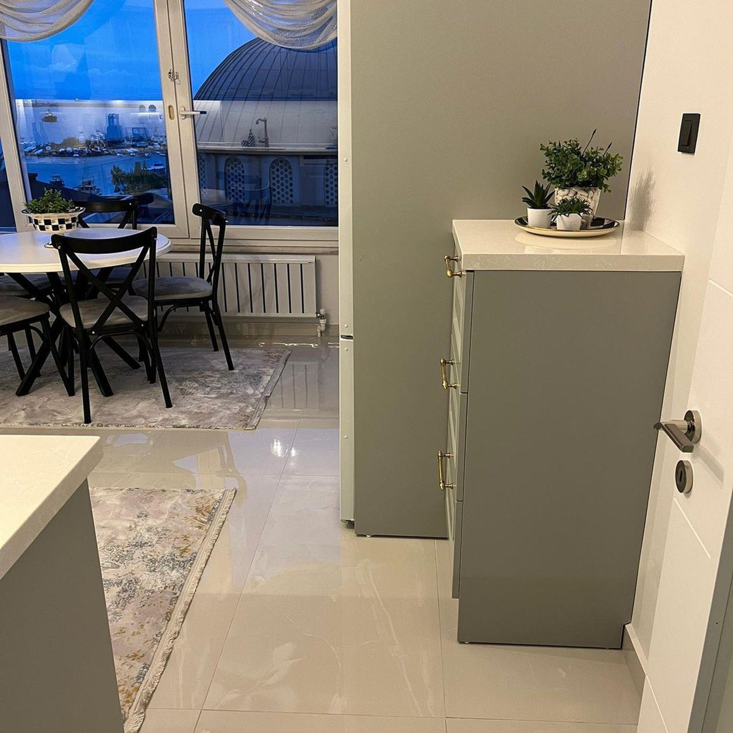 A sleek modern kitchen showcasing polished porcelain floors, minimalist furniture, and a captivating city view through the large window.