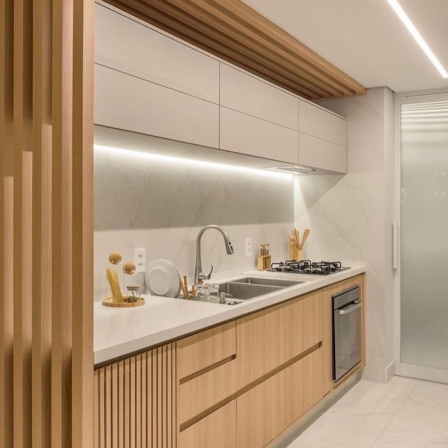 A modern kitchen with light wood cabinetry and marble backsplash