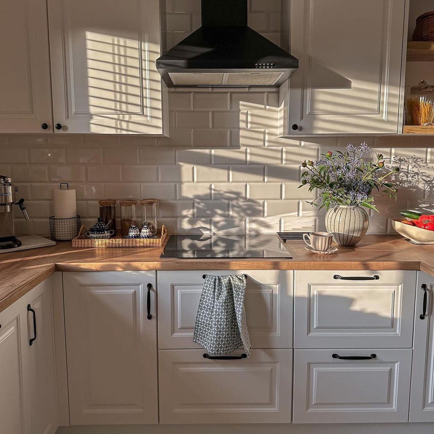 A warmly lit modern kitchen featuring cream cabinets, butcher block countertops, and a subway tile backsplash