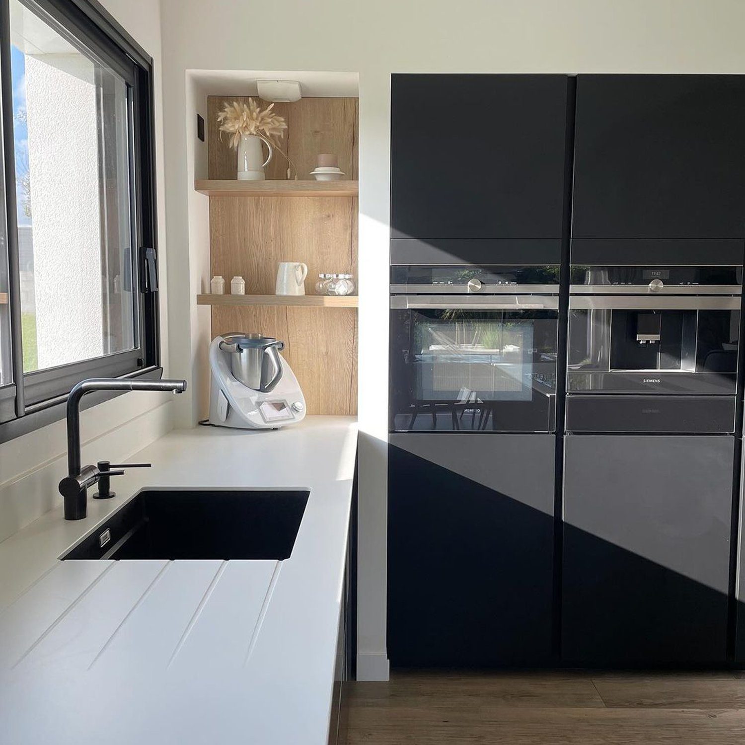 A modern kitchen featuring a sleek design with black appliances, a white countertop, and wooden accents.