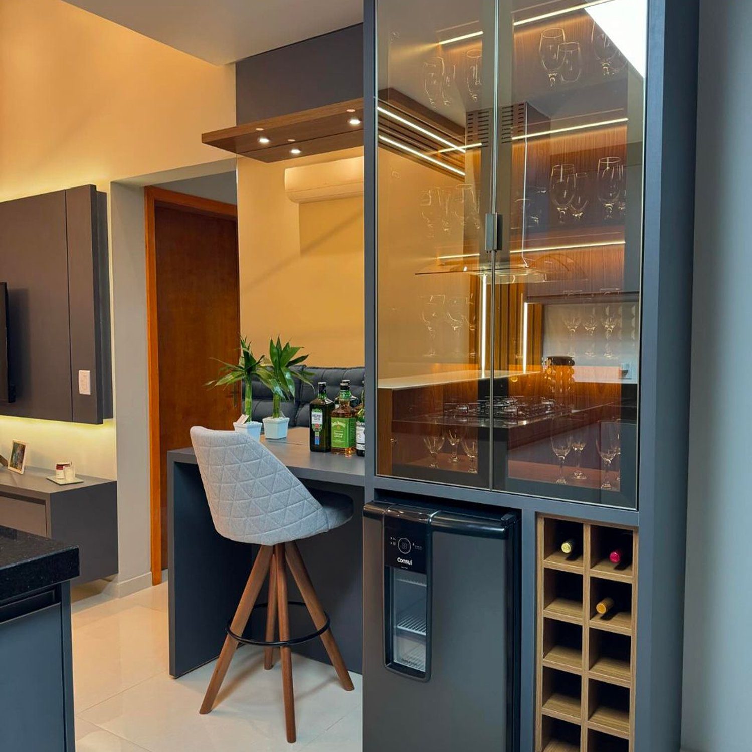 A sleek modern kitchen corner featuring a tall wine cabinet with glass doors, a built-in wine cooler, and a stylish bar stool at a dark counter.