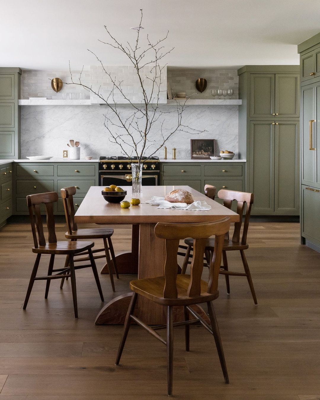 A modern kitchen with sage green cabinetry and marble countertops