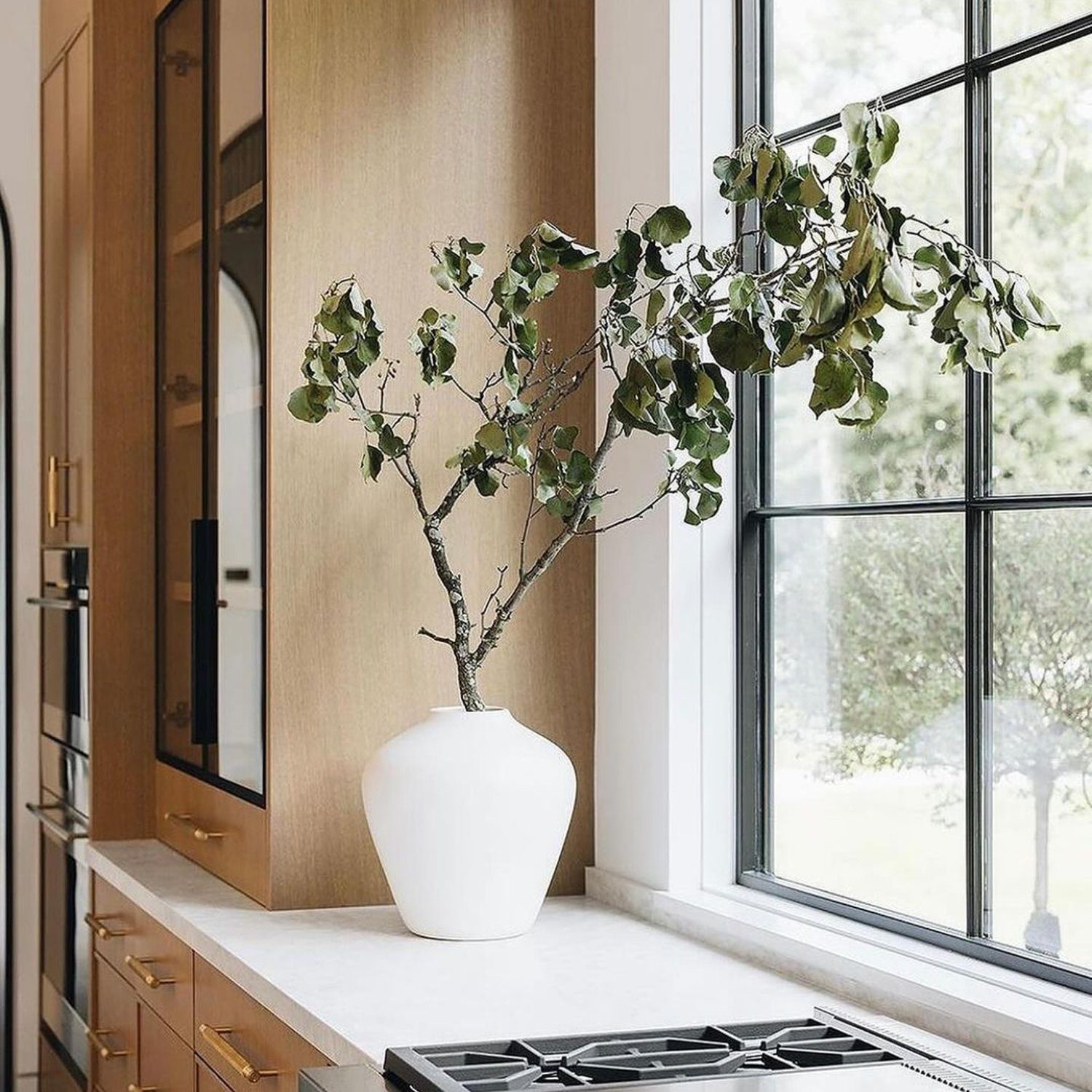 Elegant kitchen design featuring a large window with black frames, a modern gas stovetop, and brass-colored cabinetry hardware