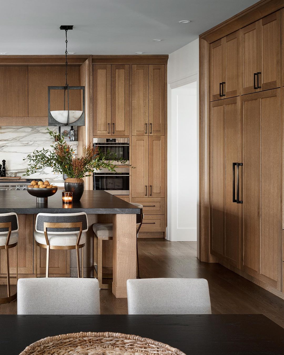 Warm and modern kitchen design featuring walnut cabinetry, sophisticated lighting fixtures, and refined natural materials.