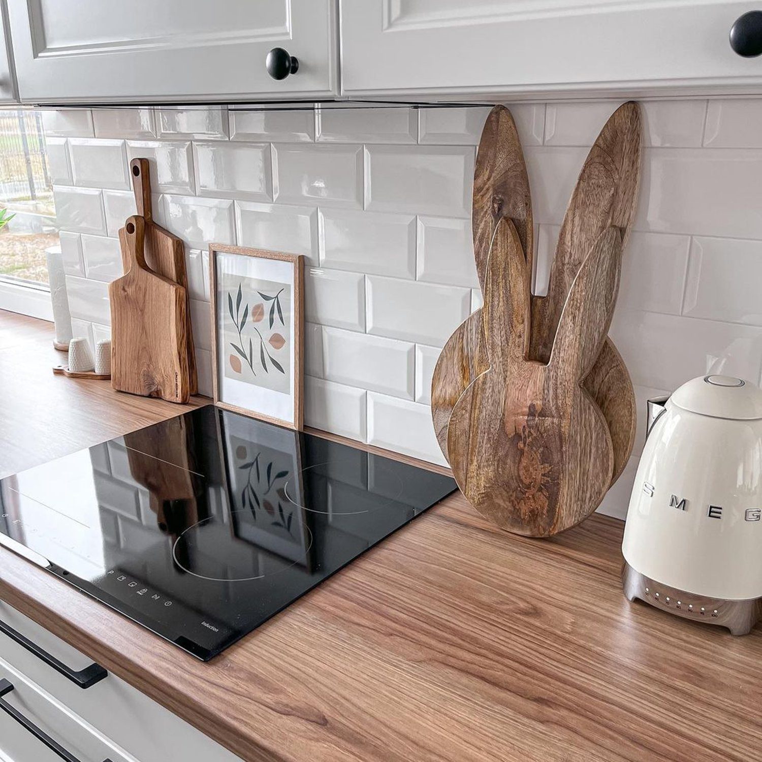 A modern kitchen featuring a wooden countertop with a built-in induction cooktop, white subway tile backsplash, and stylish kitchen accessories including a wooden bunny cutting board