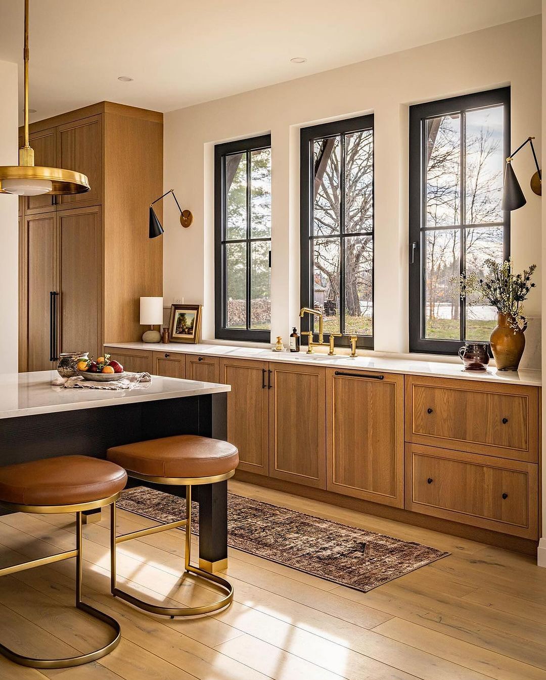 A sleek, modern kitchen space featuring rich wooden cabinetry, leather-topped stools, and black window frames with a picturesque view