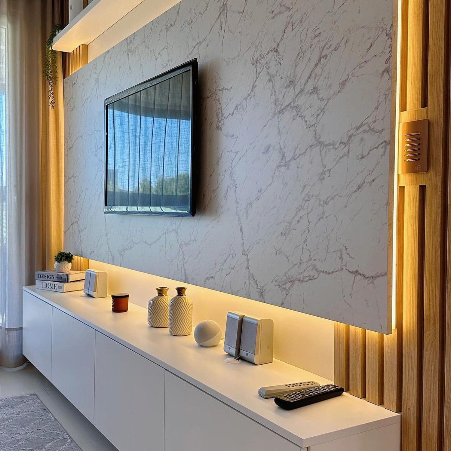 Marble patterned wall with a mounted TV and a sleek white console beneath, accentuated by warm wooden tones and decorative items.