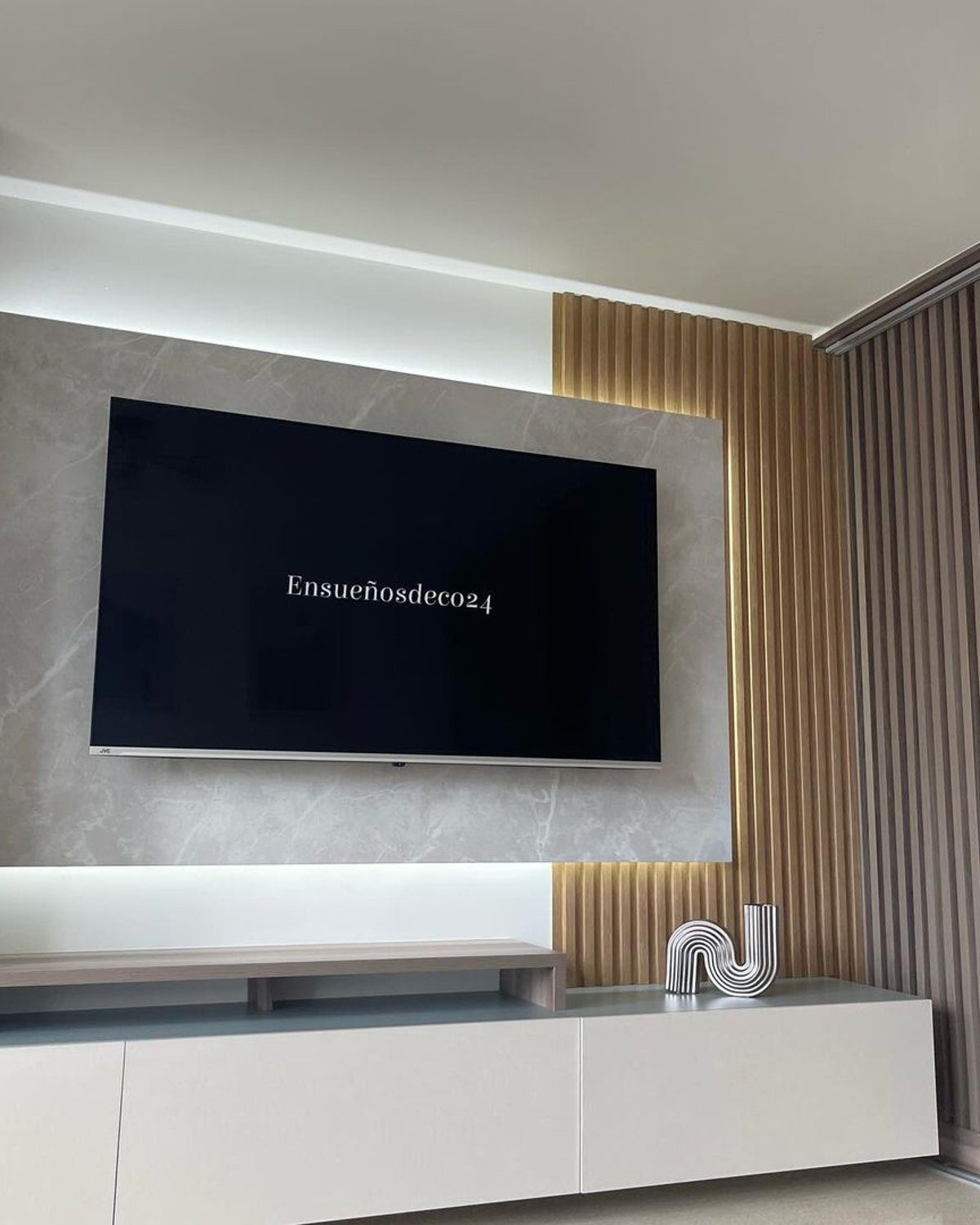 A sleek and modern living room featuring a wall-mounted flat-screen TV within a marble and wood-accented media wall