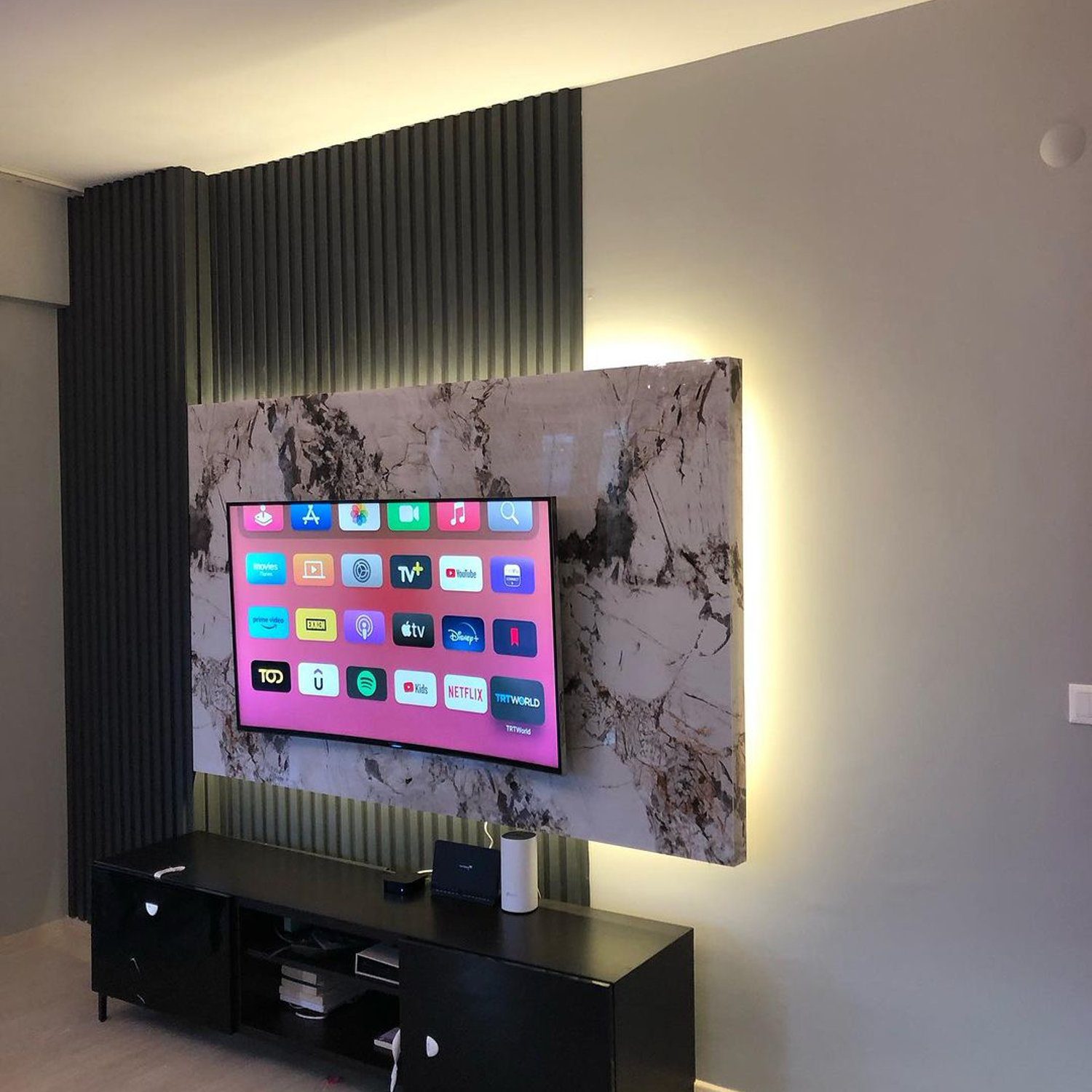 A stylishly mounted TV on a marbled patterned wall panel with ambient lighting