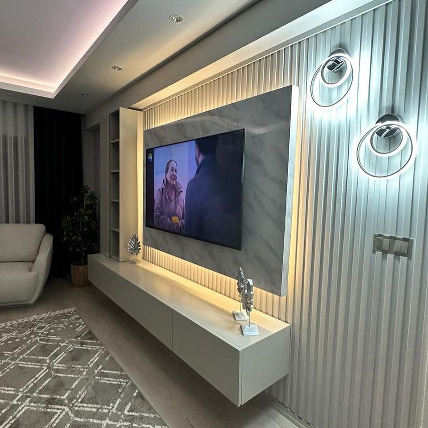 A modern living room featuring a wall-mounted TV with back lighting and a minimalist floating console.