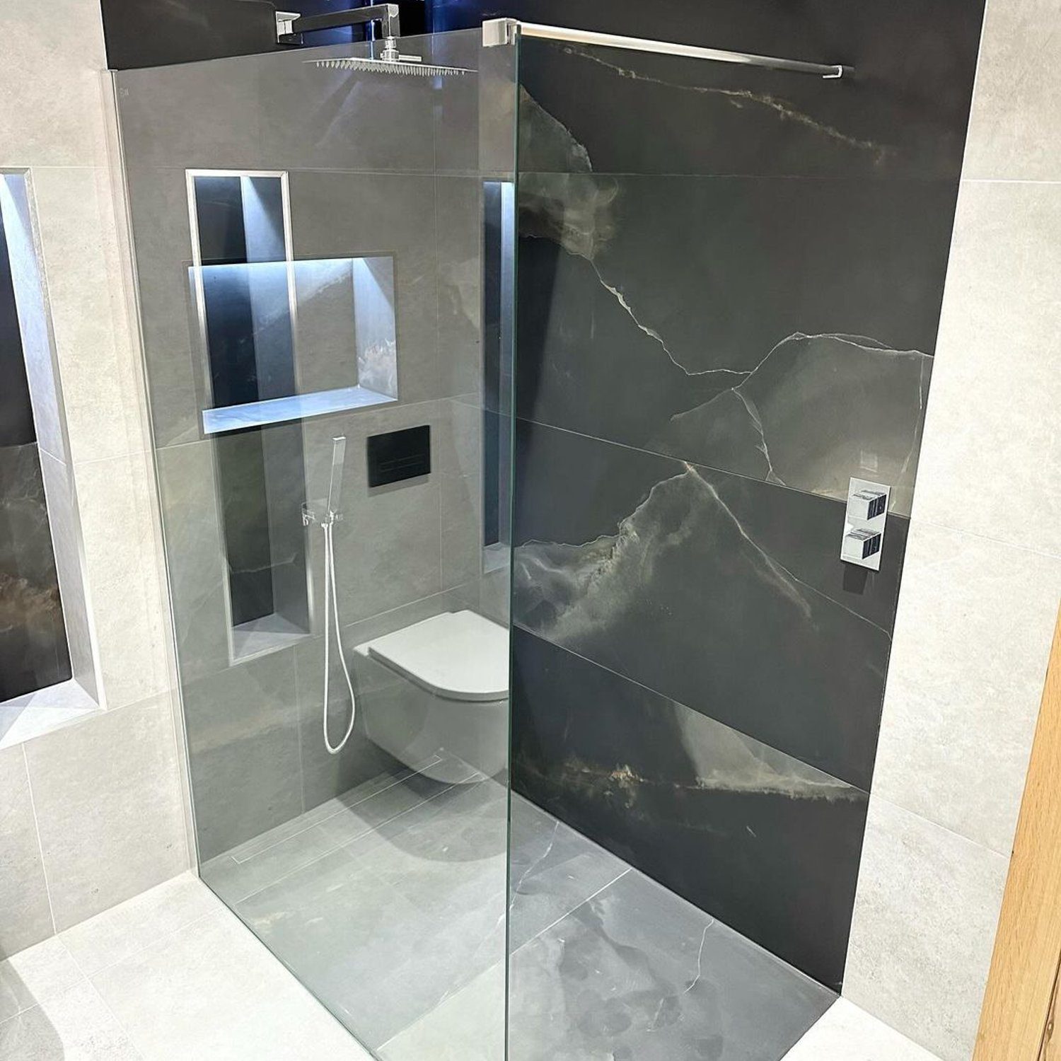 A modern bathroom with sleek dark marble walls and a glass-enclosed shower area