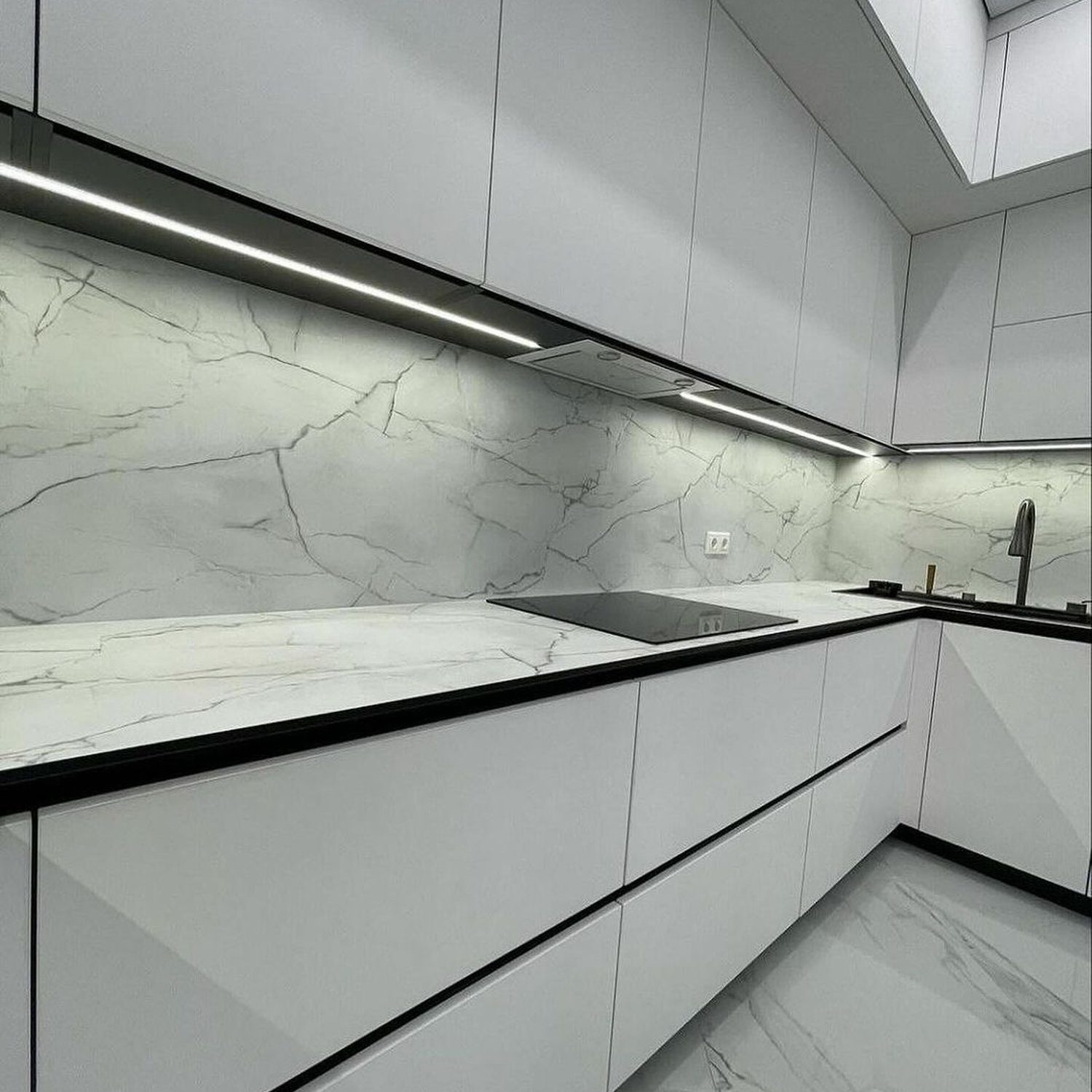 A sleek and modern kitchen featuring marble countertops, white cabinetry, and LED under-cabinet lighting