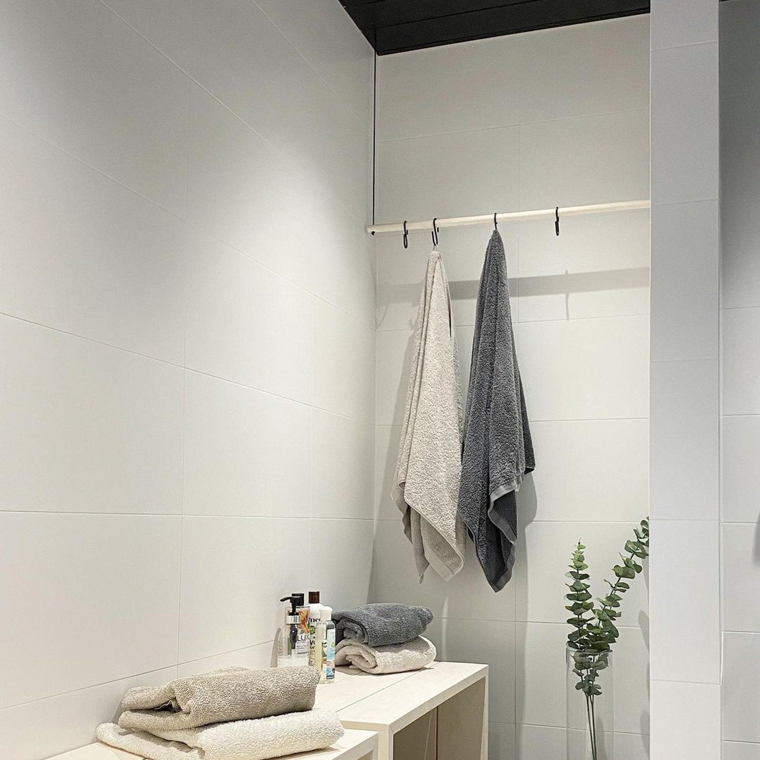 A modern minimalist bathroom design with crisp white tiles, sleek wooden bench, and contrasting black ceiling.