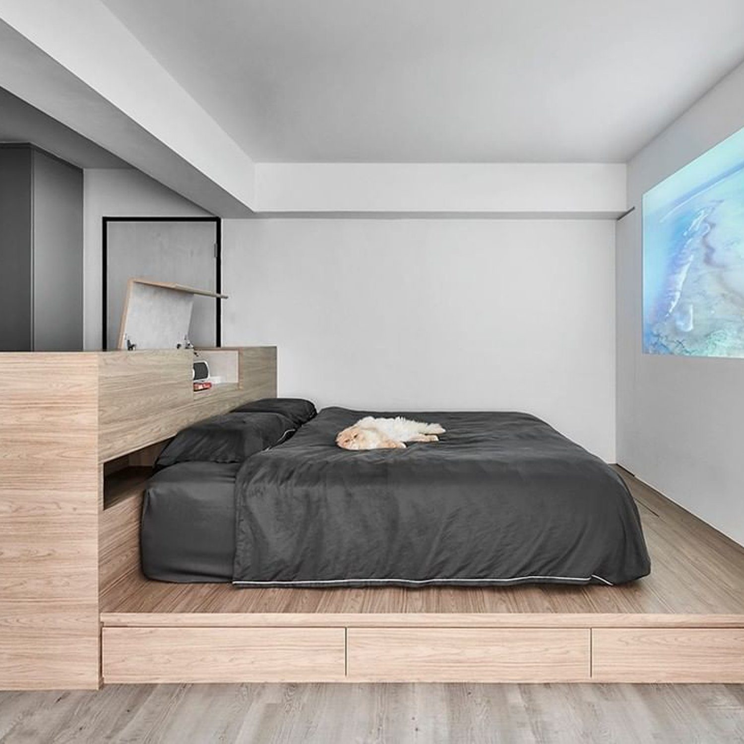 A modern minimalist bedroom with elevated wooden platform for the bed and sleek built-in furniture