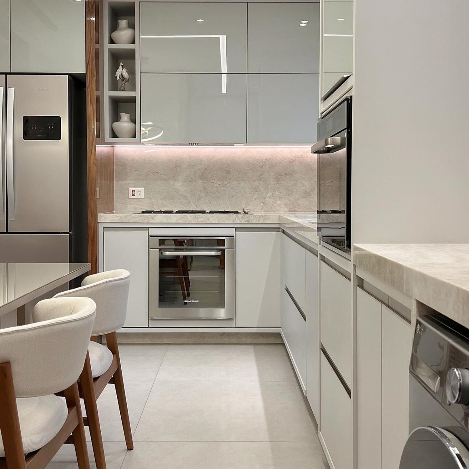 A modern minimalist kitchen featuring seamless white cabinetry, stainless steel appliances, and a warm wooden accent