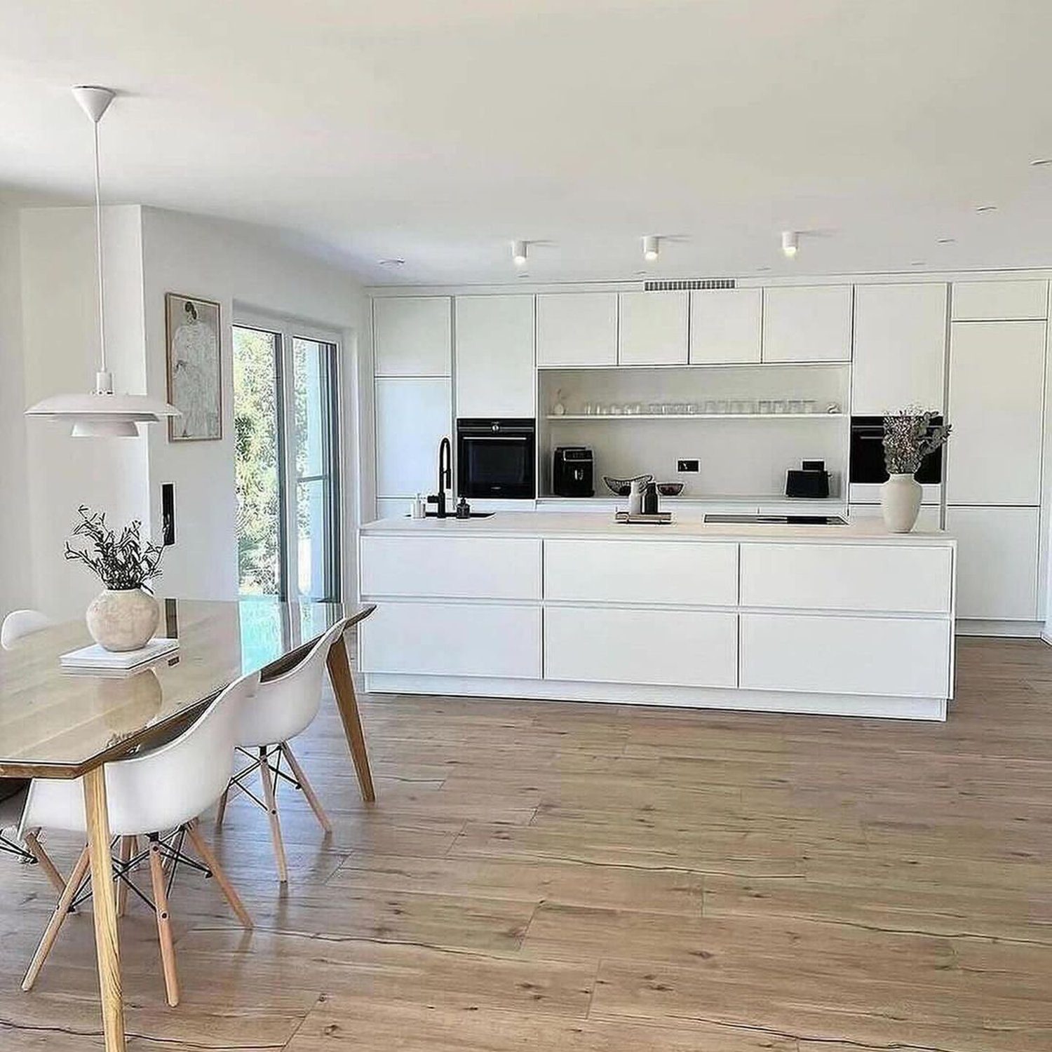 A modern minimalist kitchen with sleek white cabinetry and a warm wooden floor