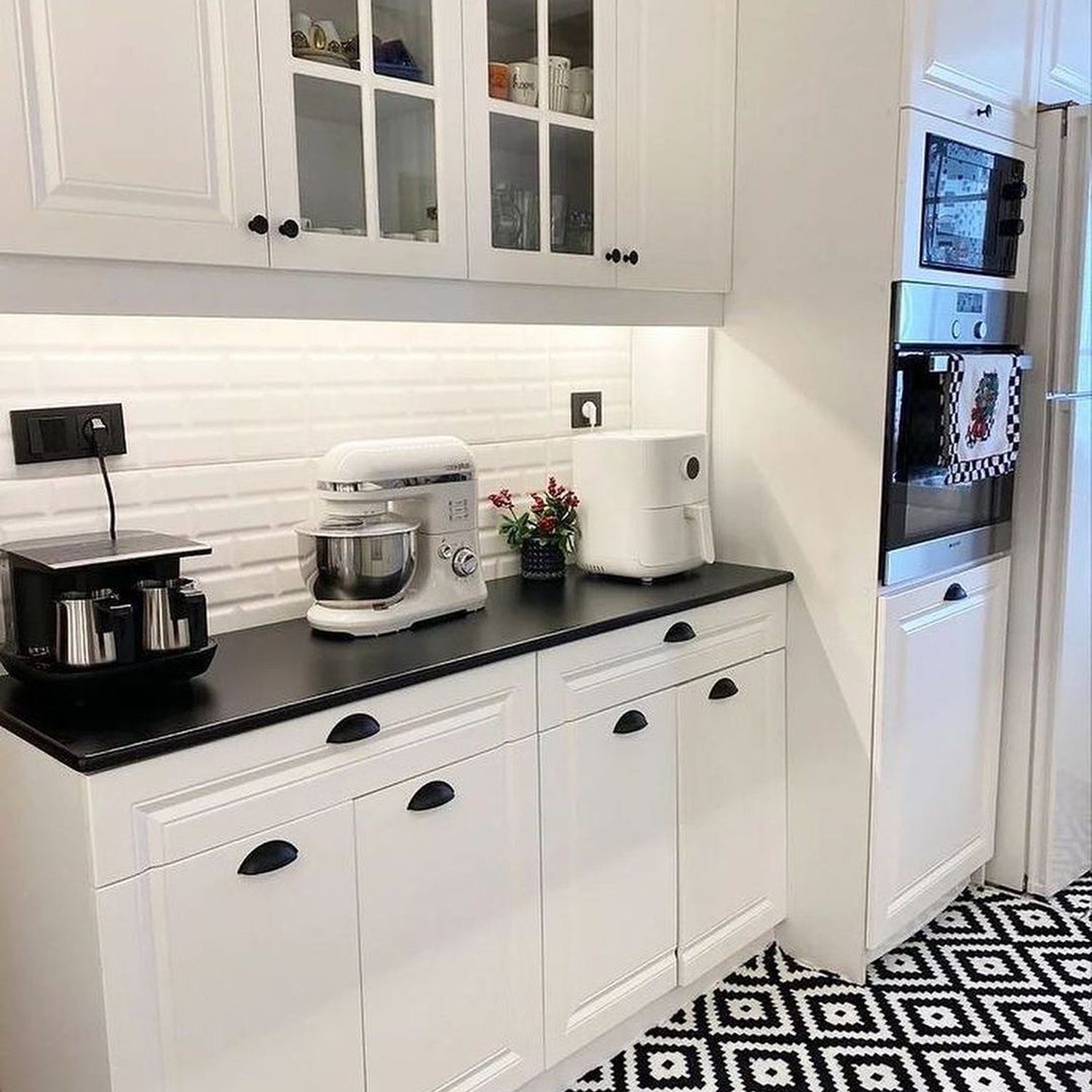 A modern, monochromatic kitchen featuring crisp white cabinetry and a contrasting black countertop, with geometric black-and-white floor tiles