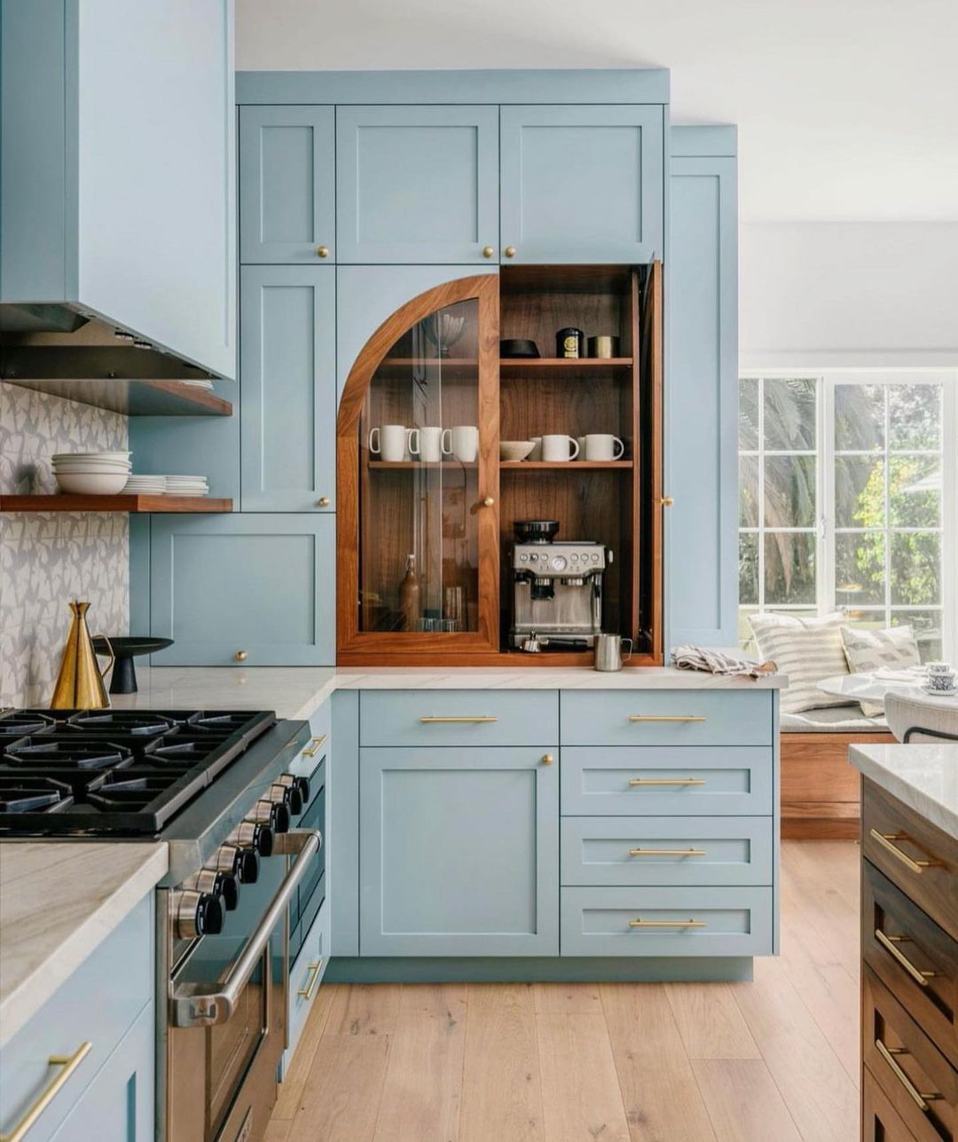 A modern kitchen featuring pale blue cabinetry, brass hardware, and a curved wooden arch detailing on the open shelving unit